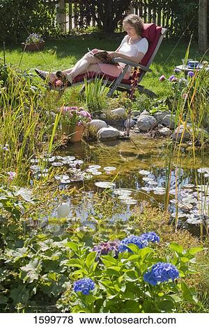 Stock Photo - Side profile of woman reading magazine on lounge chair in lawn . Fotosearch