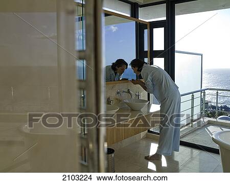 Picture - Side profile of woman washing her face in sink . Fotosearch