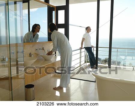 Side profile of woman washing her face in sink with her husband standing in background View Large Photo Image Stock Photograph - Side profile of woman washing her face in sink with her husband standing in background . Fotosearch