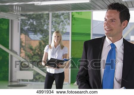 Picture - Smiling businessman with woman in background . Fotosearch