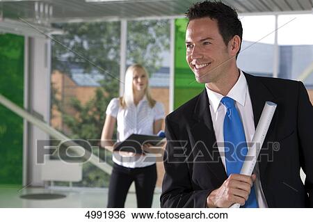 Smiling businessman with woman in background View Large Photo Image Stock Photograph - Smiling businessman with woman in background . Fotosearch