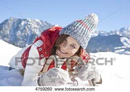 Stock Image - Smiling woman lying on toboggan, Tannheimer Tal, Tyrol, Austria . Fotosearch
