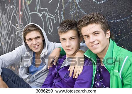 Stock Photo - Three boys sitting side by side in front of a wall, close-up . Fotosearch