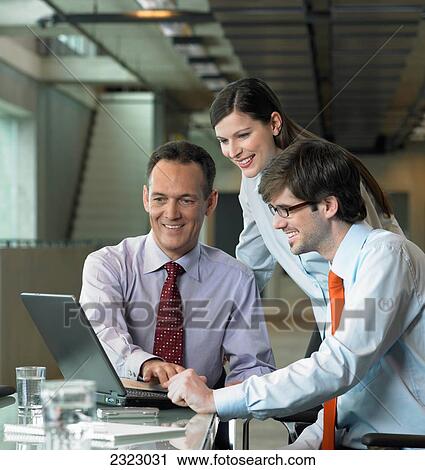Stock Image - Three businesspeople looking at laptop in office . Fotosearch