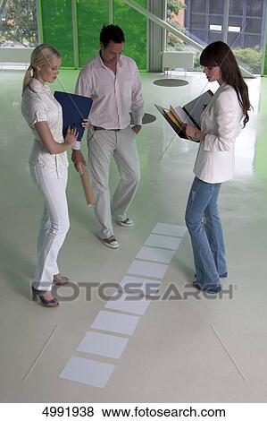 Three businesspeople looking at documents on office floor View Large Photo Image Stock Photo - Three businesspeople looking at documents on office floor . Fotosearch