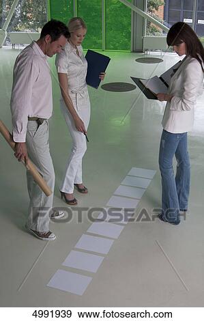 Three businesspeople looking at documents on office floor View Large Photo Image Stock Photo - Three businesspeople looking at documents on office floor . Fotosearch