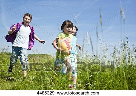 Three children running with football over a meadow View Large Photo Image Stock Photo - Three children running with football over a meadow . Fotosearch