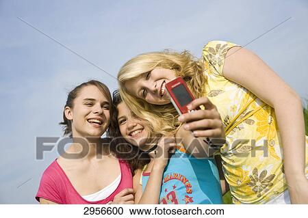 Stock Image - Three young girls are taking photos of themselves, low angle view . Fotosearch