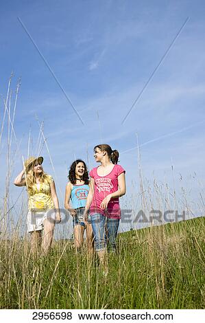 Three young girls walking through a meadow, low angle view View Large Photo Image Stock Photo - Three young girls walking through a meadow, low angle view . Fotosearch