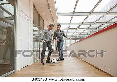 Stock Image - Two business men playing soccer in office building . Fotosearch