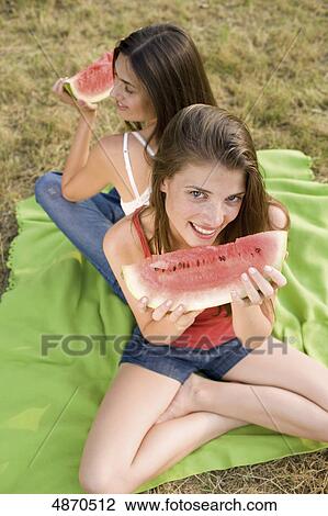 Stock Image - Two young women eating melons outdoors . Fotosearch