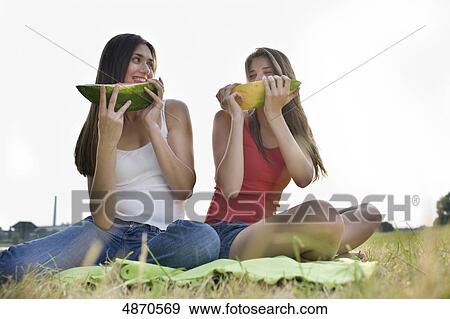 Stock Photo - Two young women eating melons outdoors . Fotosearch