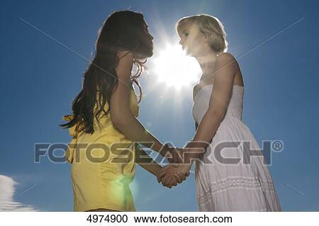 Two young women hand in hand under blue sky View Large Photo Image Stock Image - Two young women hand in hand under blue sky . Fotosearch