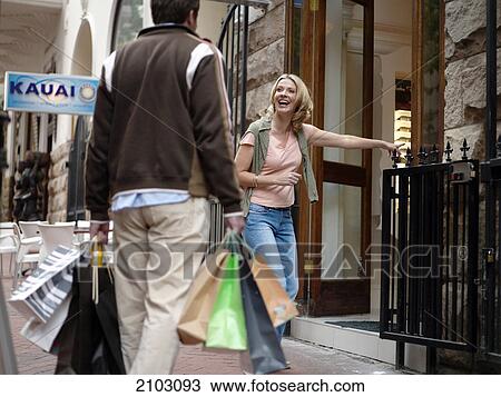 Stock Image - Woman looking at man carrying shopping bags . Fotosearch