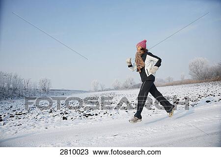 Stock Image - Woman running in snow covered landscape . Fotosearch