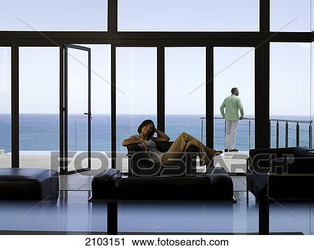 Woman sitting in armchair with man standing in background View Large Photo Image Stock Image - Woman sitting in armchair with man standing in background . Fotosearch
