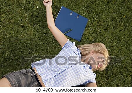 Young blond woman lying in grass next to file folder View Large Photo Image Stock Image - Young blond woman lying in grass next to file folder . Fotosearch