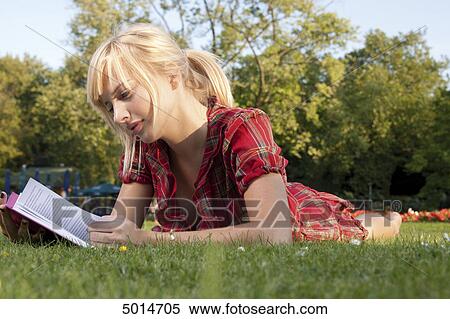 Stock Photography - Young blond woman reading book in grass . Fotosearch