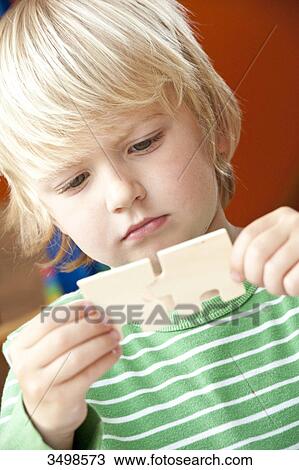 Stock Image - Young boy holding two jigsaw pieces, low angle view . Fotosearch