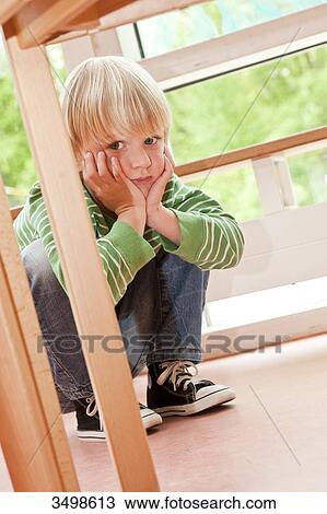 Young boy squatting beside a table and holding head in hands, low angle view View Large Photo Image Stock Image - Young boy squatting beside a table and holding head in hands, low angle view . Fotosearch
