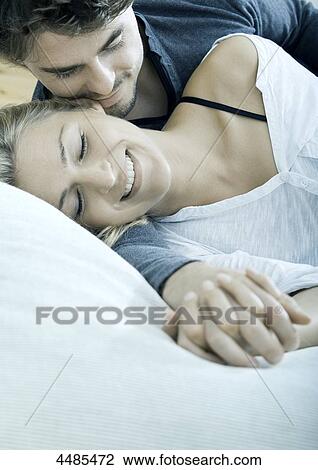 Stock Image - Young couple lying hand in hand in bed . Fotosearch