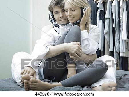 Stock Photo - Young couple on bed listening to music with headphones . Fotosearch
