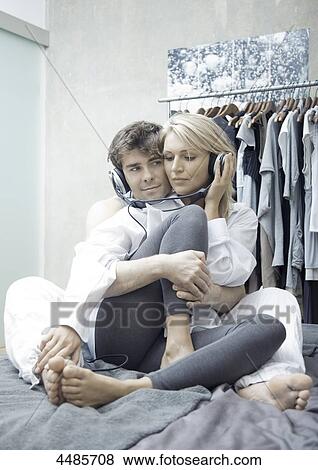 Stock Photo - Young couple on bed listening to music with headphones . Fotosearch