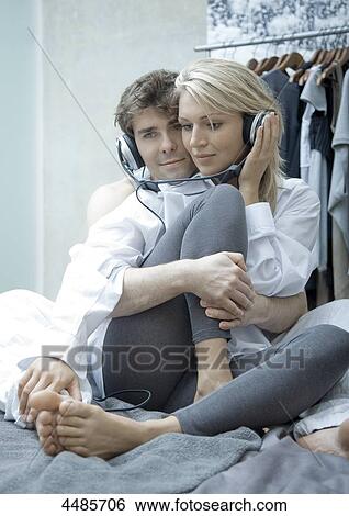 Stock Photograph - Young couple on bed listening to music with headphones . Fotosearch