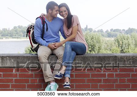 Stock Image - Young couple sitting on wall . Fotosearch