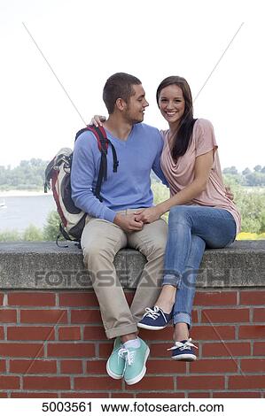 Stock Image - Young couple sitting on wall . Fotosearch