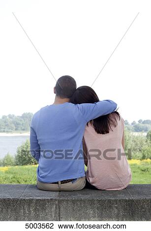 Stock Image - Young couple sitting on wall . Fotosearch