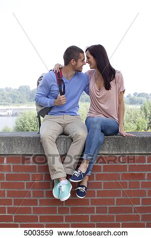 Stock Photo - Young couple sitting on wall . Fotosearch