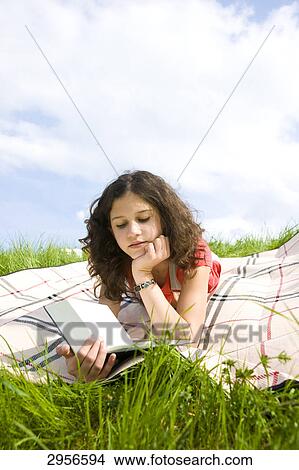 Picture - Young girl lying on a blanket, reading in a book, low angle view . Fotosearch