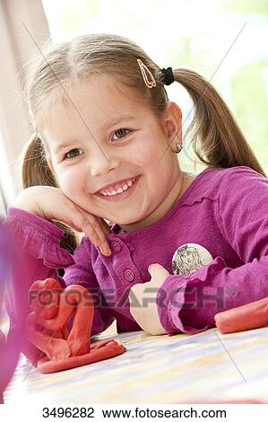 Stock Image - Young girl sitting at a table with a figure made of plasticine, low angle view . Fotosearch