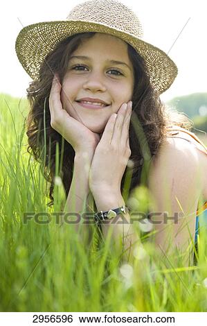 Young girl with straw hat lying in a rich green meadow, eye contact View Large Photo Image Stock Photograph - Young girl with straw hat lying in a rich green meadow, eye contact . Fotosearch