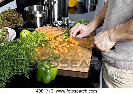 Stock Image - Young man cutting carrots in kitchen . Fotosearch