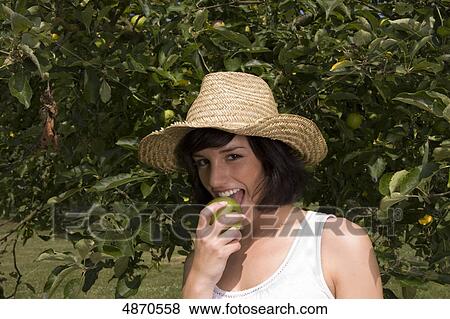 Stock Photo - Young woman eating apple from tree, portrait . Fotosearch
