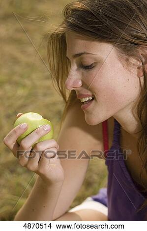 Young woman eating apple in meadow View Large Photo Image Picture - Young woman eating apple in meadow . Fotosearch