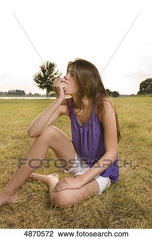Stock Image - Young woman eating fruit in meadow . Fotosearch