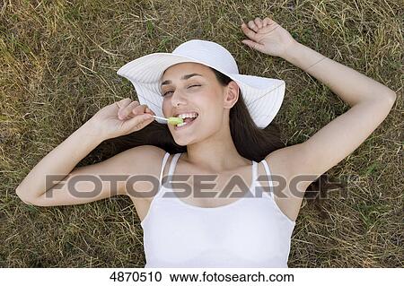Young woman eating lolly in meadow View Large Photo Image Stock Image - Young woman eating lolly in meadow . Fotosearch