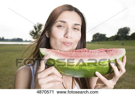 Stock Image - Young woman eating melon outdoors . Fotosearch