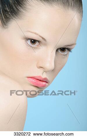 Stock Image - Young woman in front of blue backgound, portrait . Fotosearch