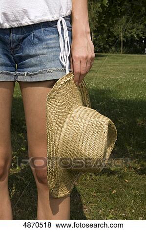 Stock Photo - Young woman in shorts and straw hat in meadow . Fotosearch