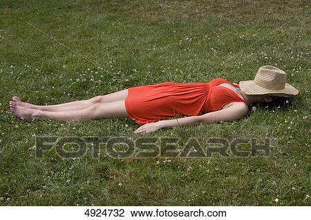 Stock Image - Young woman lying in meadow with straw hat covering her face . Fotosearch