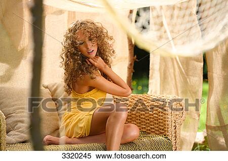 Stock Photography - Young woman sitting on a couch in a tent, low angle view . Fotosearch