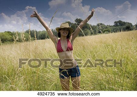 Stock Photography - Young woman standing in meadow with arms outstretched . Fotosearch