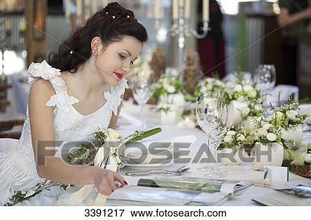 Bride sitting at a table, looking in a magazine View Large Photo Image Stock Photo - Bride sitting at a table, looking in a magazine . Fotosearch