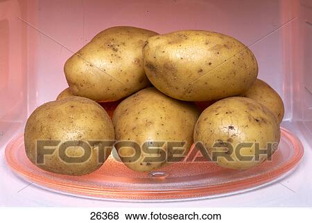 Stock Photo - Close-up of raw potatoes in a microwave oven . Fotosearch