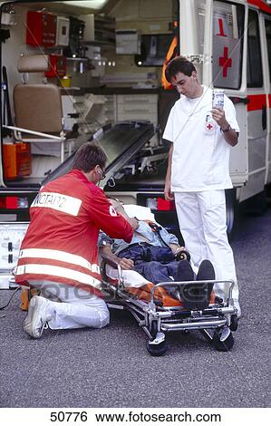Stock Photograph - Doctor examining patient on stretcher in front of an ambulance . Fotosearch