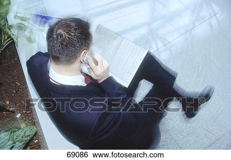 High angle view of businessman talking on mobile phone while reading financial newspaper View Large Photo Image Stock Photograph - High angle view of businessman talking on mobile phone while reading financial newspaper . Fotosearch